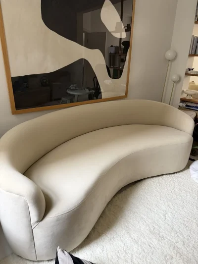 Large beige curved upholstered sofa with wraparound back